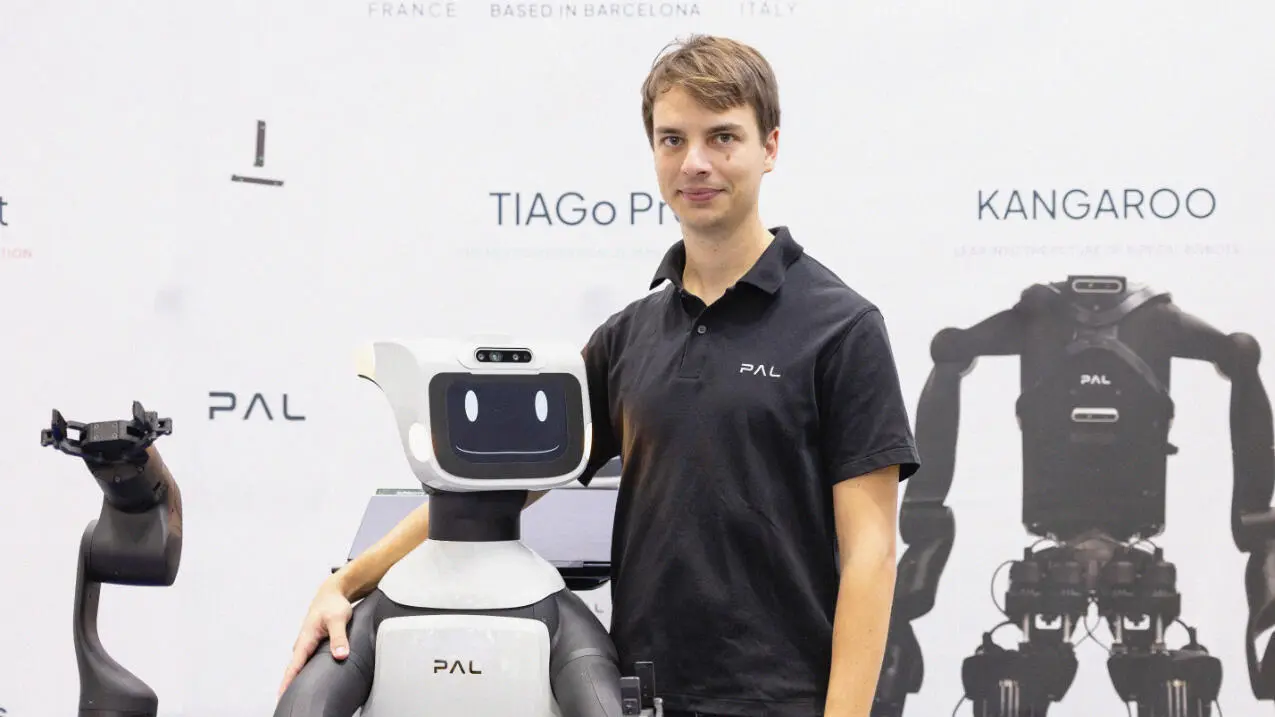 Thomas with his arm around a robot, facing the camera