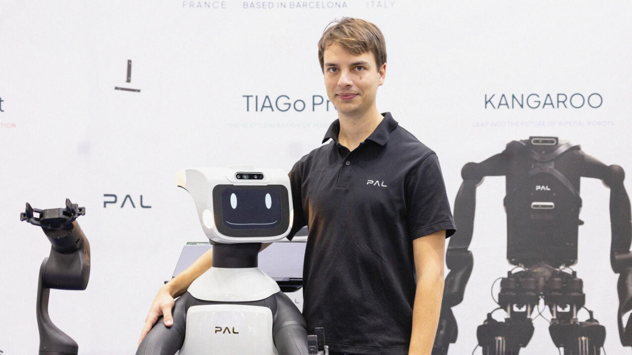 Thomas with his arm around a robot, facing the camera